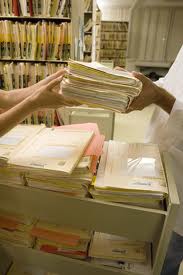 A filing cabinet that's open and one person is handing a stack of folders/files to another. Increased Audits Could Equal A Streamlined Response for Healthcare Organizations