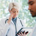Senior woman, doctor and headache in burnout, grief or mistake with digital report in hospital buil